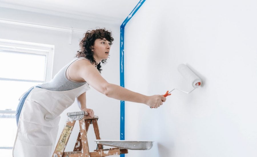 woman standing on ladder to paint a wall