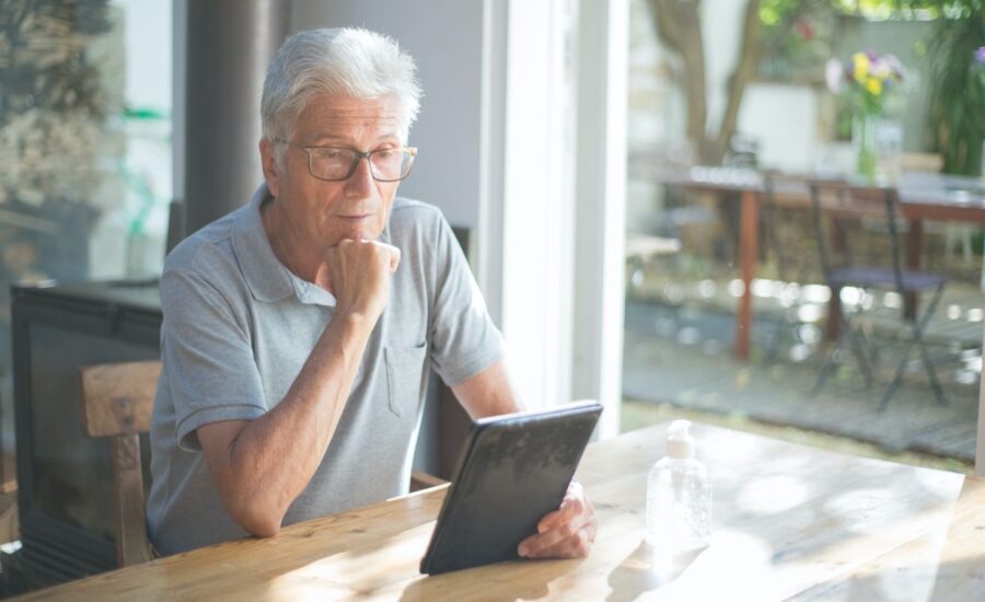 A man is seen sitting at a table looking at his ipad