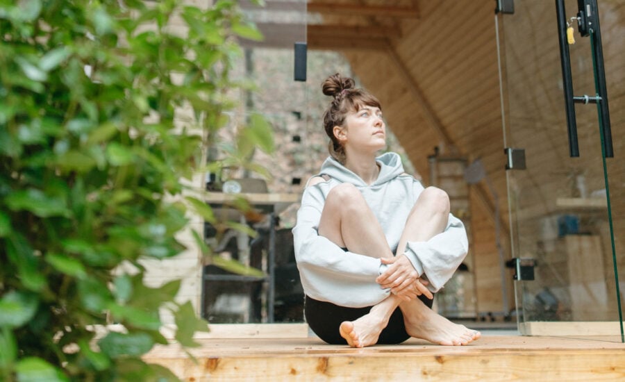 A woman alone on the porch of her cottage, looking up as she's deep in thought.