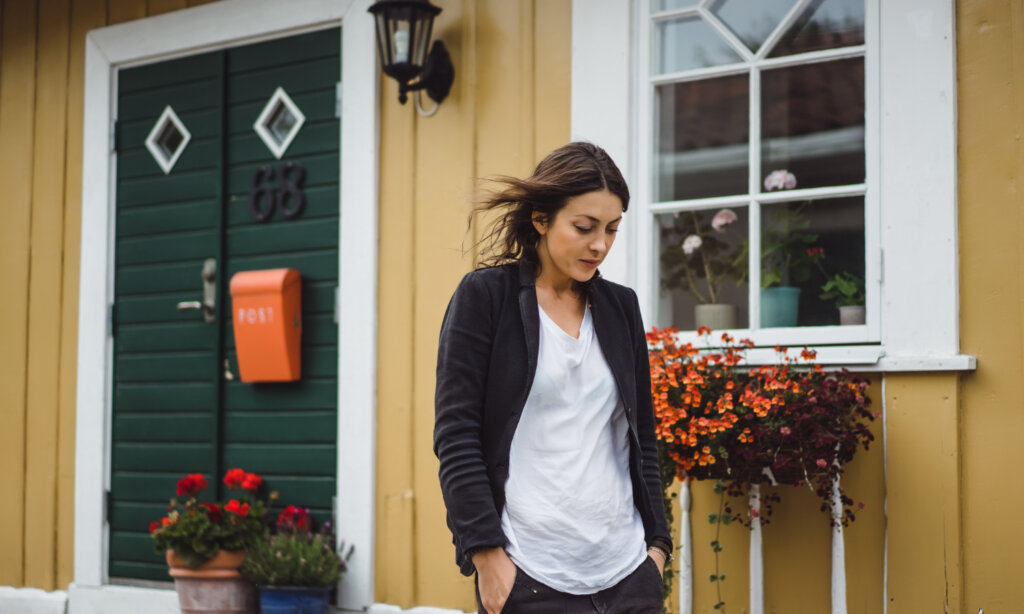 A young woman stands outside a house