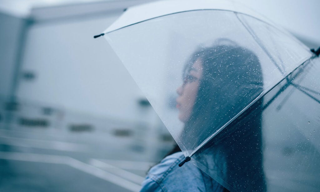 A woman stands under an umbrella in the rain