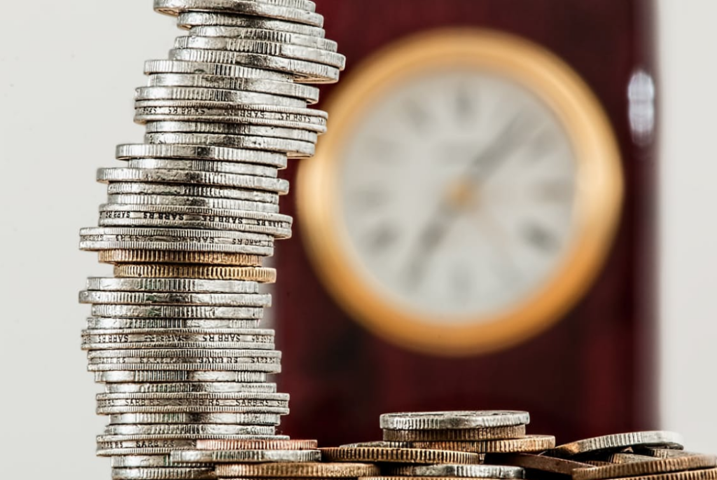 Clock in the background with a stack of coins. Time your earnings to minimize taxes