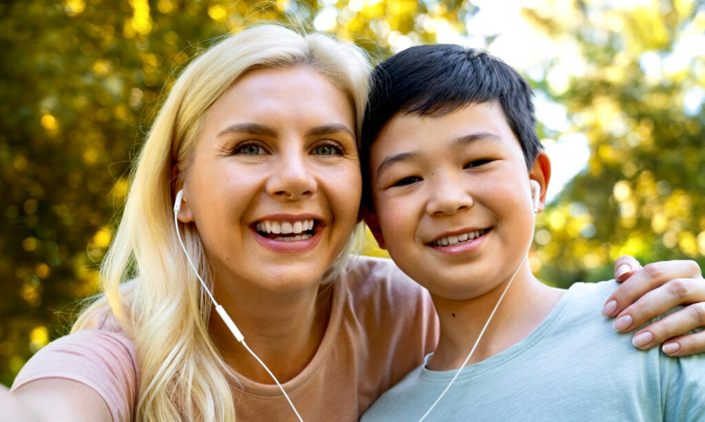 A mother and her young son smile and share a pair of earbuds