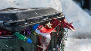 a large plastic trashbin overflowing with garbage and discarded Christmas paper lights bows etc