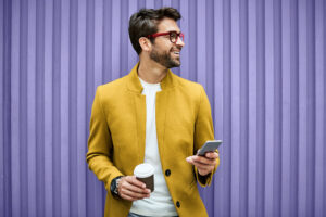 man smiling as he's using his phone and having a coffee