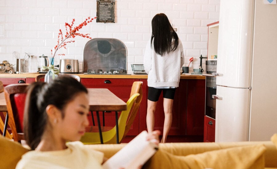 Mom reading on the couch while the daughter is fixing a snack in the kitchen of their Airbnb rental