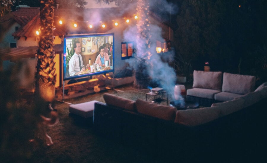 The ultimate backyard fire pit, surrounded by an outdoor sectional sofa and a big movie screen