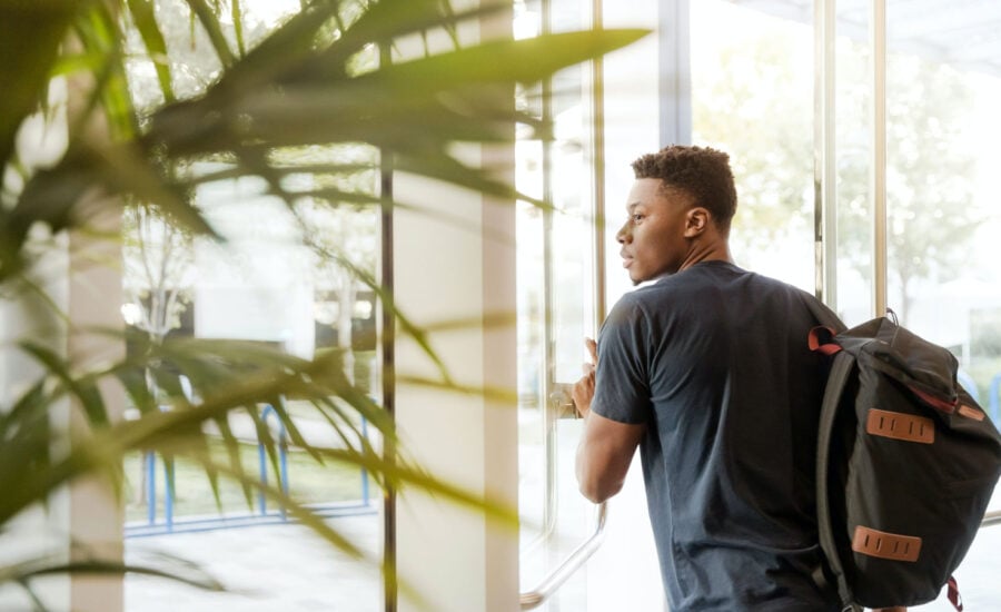 A student walking out of a building, thinking about his financial situation