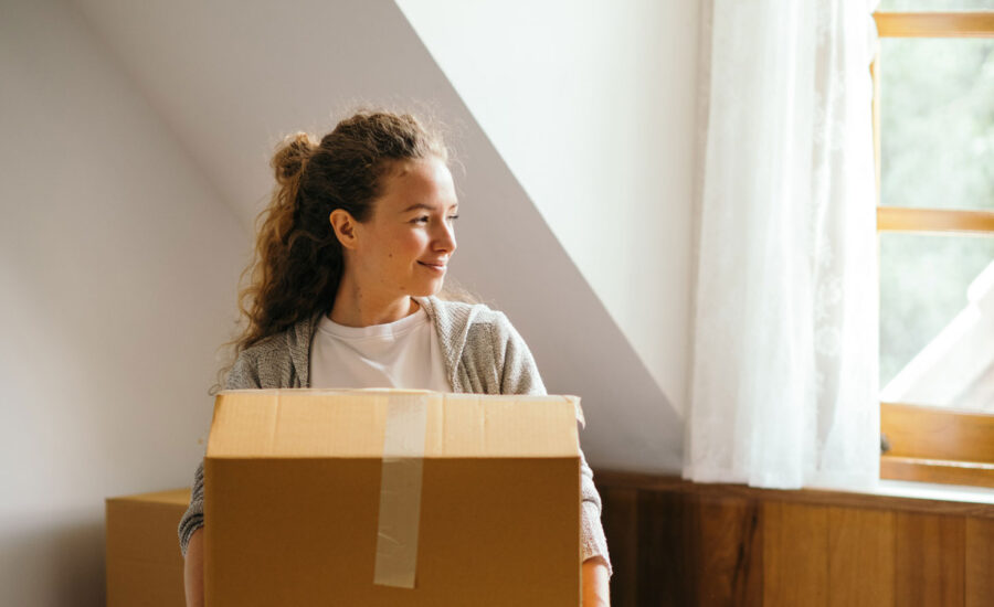 A woman holding a box as she moves into her first apartment