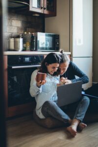 Couple sitting on kitchen floor looking at laptop