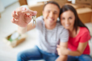 Close-up of man's hand holding house keys with soft focus couple in background
