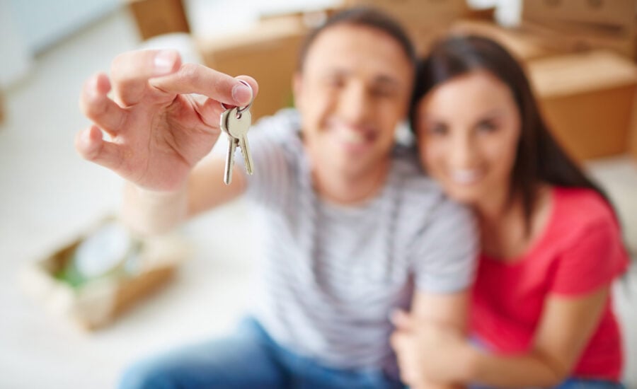 Close-up of man's hand holding house keys with soft focus couple in background