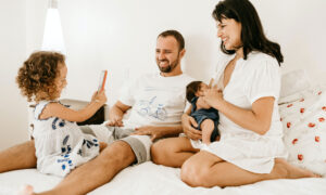 A young family sitting together on a bed laughing, 'cause life's good!