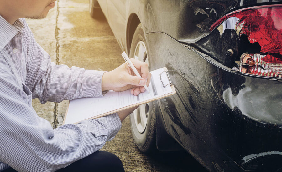 An adjustor knelt and taking notes based on the damage of the rear lights of a car.