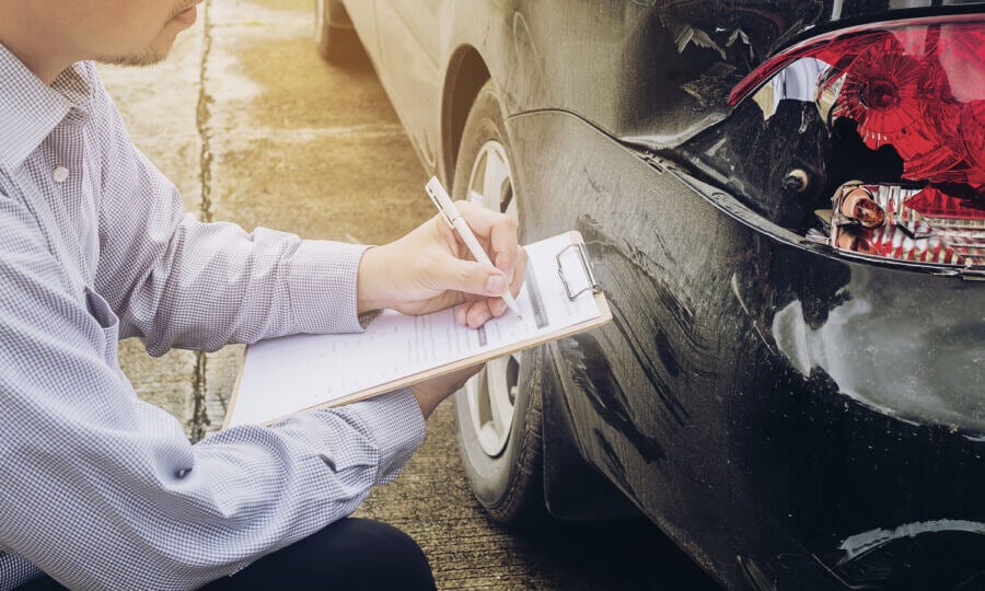 An adjustor knelt and taking notes based on the damage of the rear lights of a car.