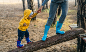 A small child walking up a log with his mom holding his hand