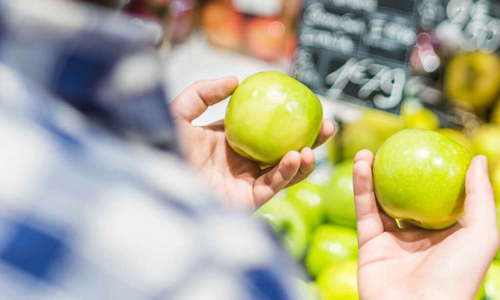 A man shopping in the produce aisle, deciding between two apples