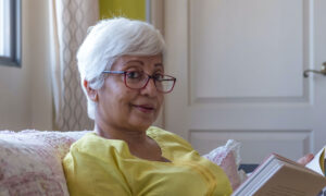 An older woman on her couch, reading a book.