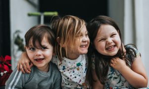 Three young children smile and hug each other