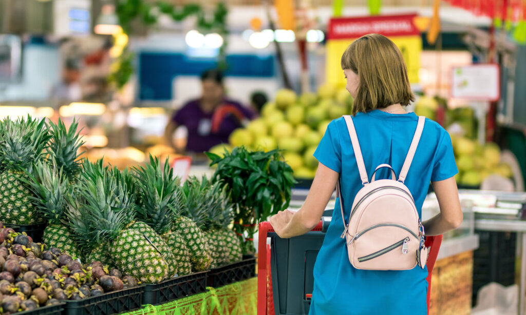 A woman in the fruit section of the grocery aisle in front of a stand of pineapples