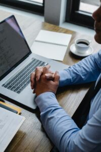 man's hands folded over laptop computer