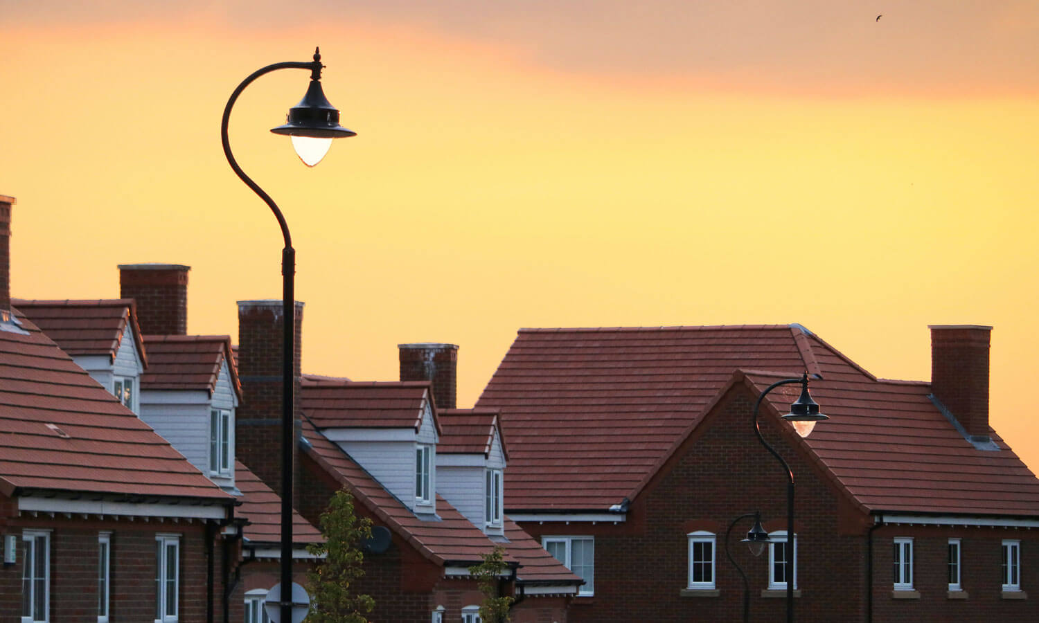 The sun is setting on a row of houses on a suburban street.