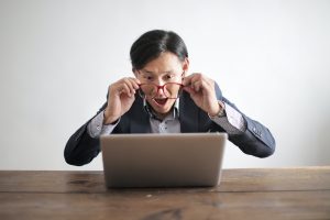 Man with glasses looking surprised at computer monitor