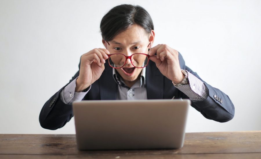 Man with glasses looking surprised at computer monitor