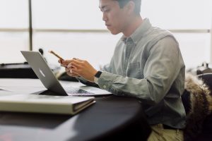 man looking concerned while reading on mobile phone and laptop