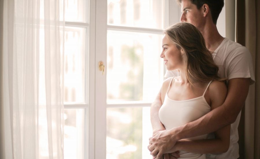 young couple looks out window of their home after purchasing home insurance