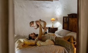 A father and a baby playing together on a bed at the cottage.