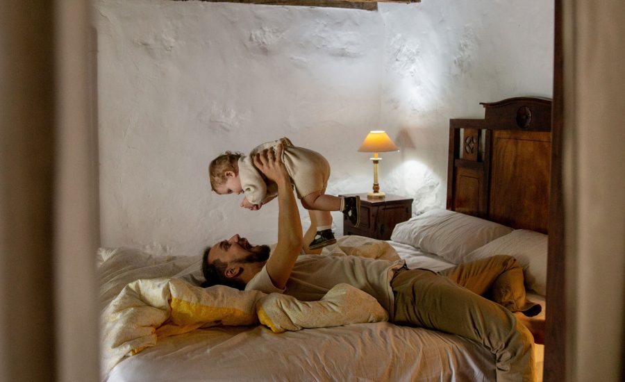 A father and a baby playing together on a bed at the cottage.