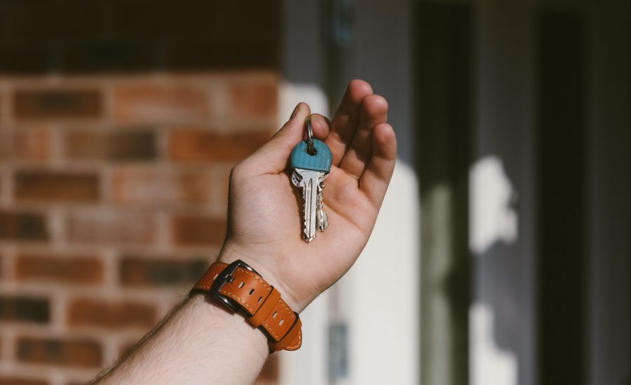 close-up of hand holding keys with home in background