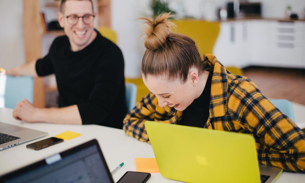 Two people laughing as they work on their computers