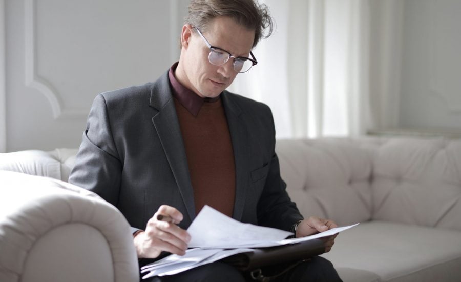 man sitting on couch reading paperwork