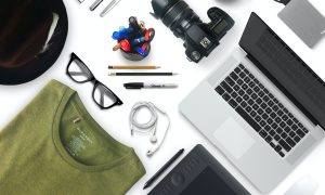 A flat lay of items you may own, including a tablet, computer, camera, phone, glasses and more.