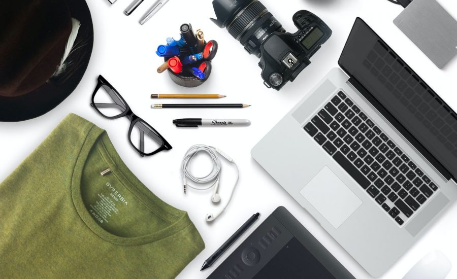 A flat lay of items you may own, including a tablet, computer, camera, phone, glasses and more.