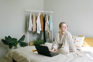 A young woman sits on her bed, compares home insurance quotes on her computer