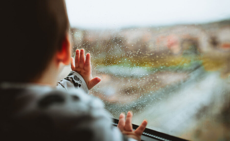 A baby touching a rain-drenched window.