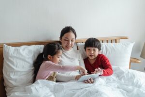 mother and children reading tablet in bed