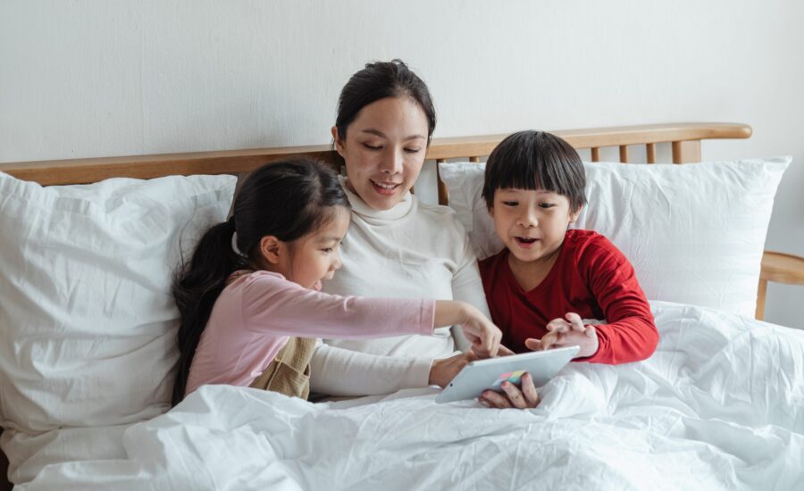 mother and children reading tablet in bed