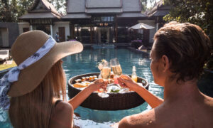 a couple by the resort pool clinking glasses of champagne during a vacation they've ben waiting for.