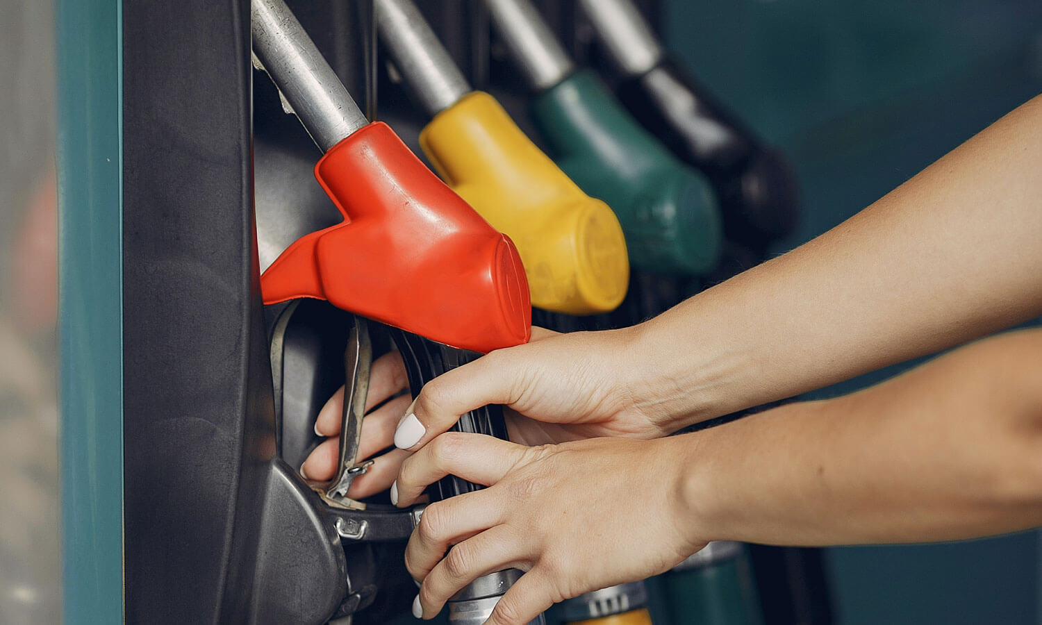A pair of hands reaching for the gas pump at a station
