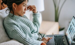 A woman holds a credit card while looking at her laptop.