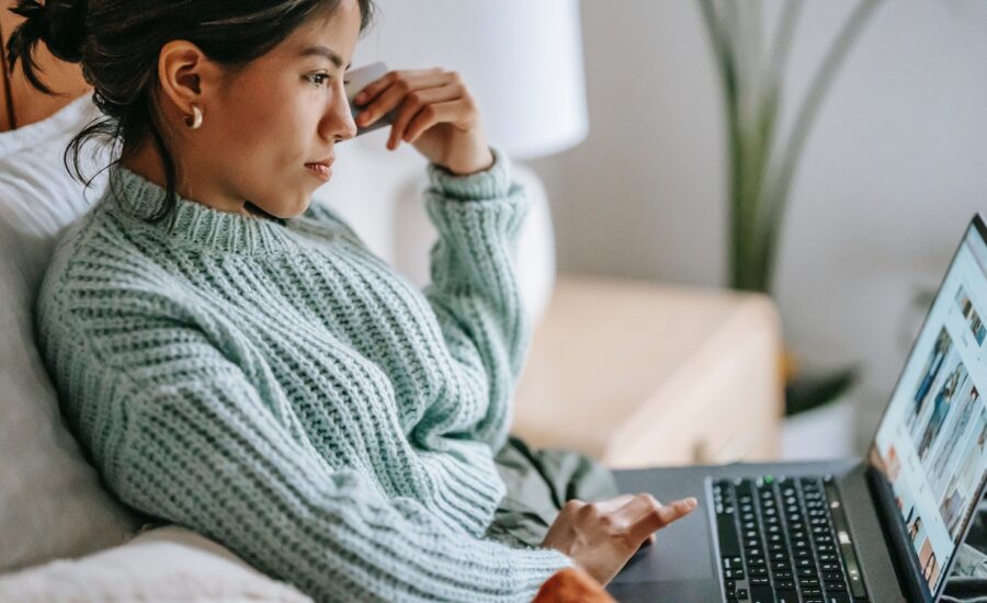 A woman holds a credit card while looking at her laptop.