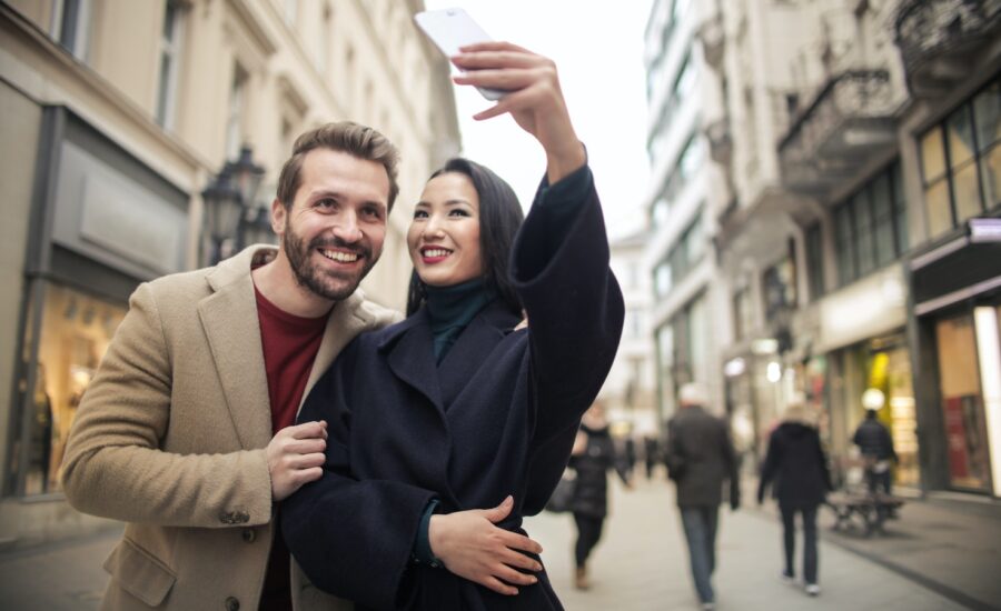 A man and woman take a selfie on a city street.