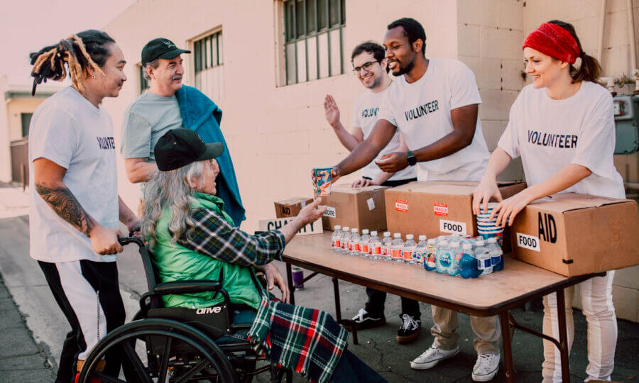 Five people are seen in a photo giving food to a man in a wheel chair