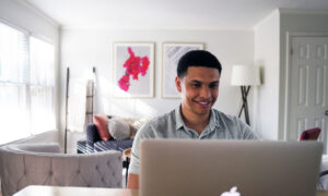 A man sitting in his living room, smiling as he checks his investments on his computer.