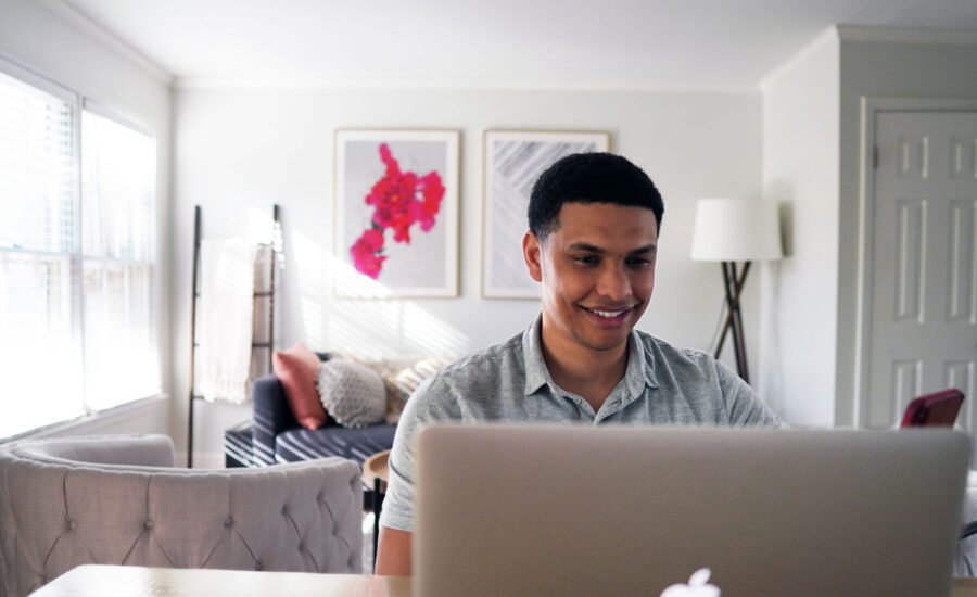 A man sitting in his living room, smiling as he checks his investments on his computer.