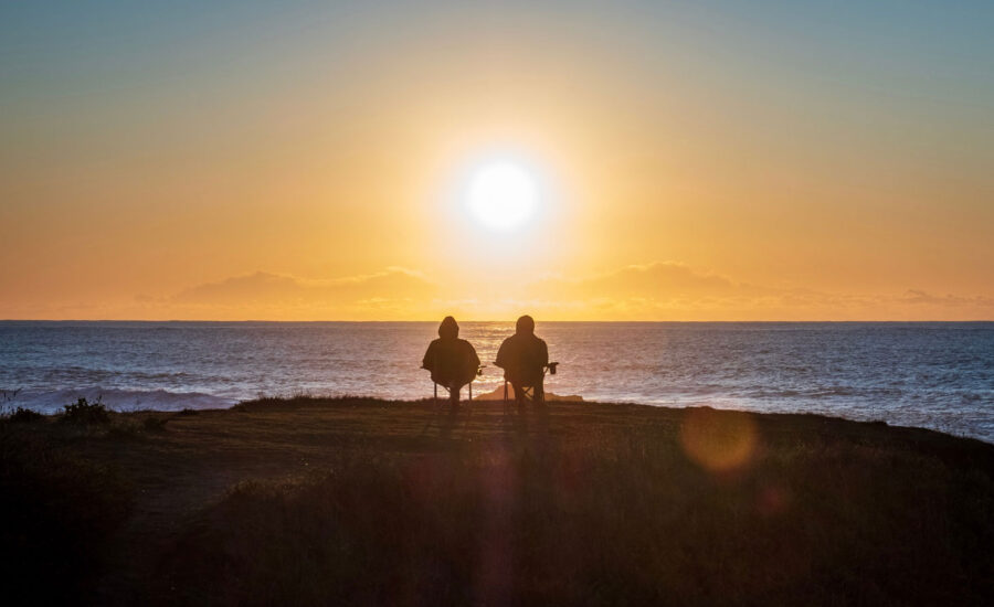 Two people sitting along the water, as the sun goes down.